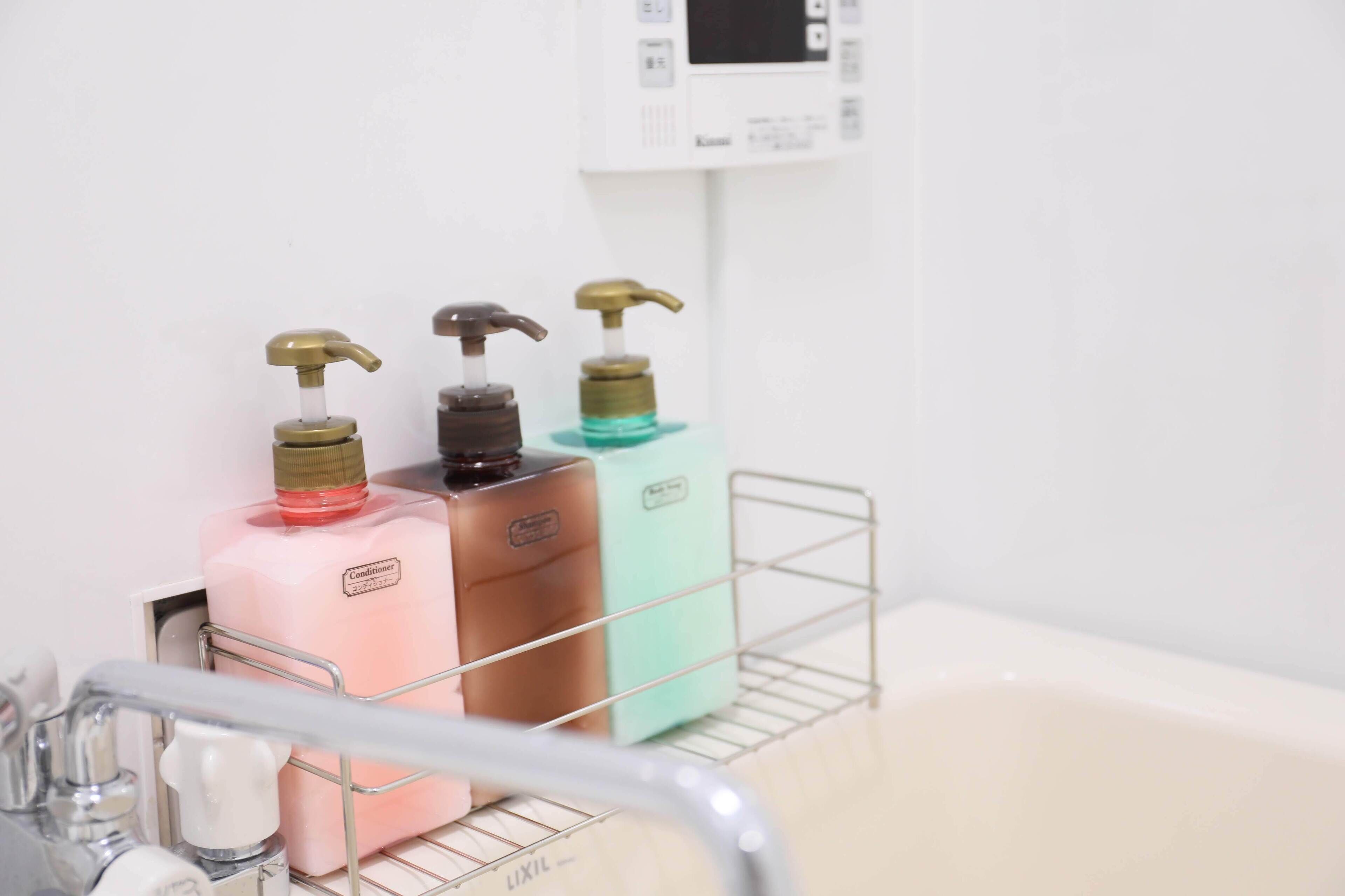 Une salle de bain avec un étagère en métal sur laquelle sont posées trois bouteilles de savon liquide, un robinet et un panneau de commande fixé au mur.