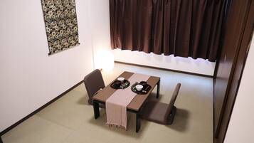Un comedor con una mesa dispuesta para dos personas, una silla, un banco y una lámpara fijada en la pared.