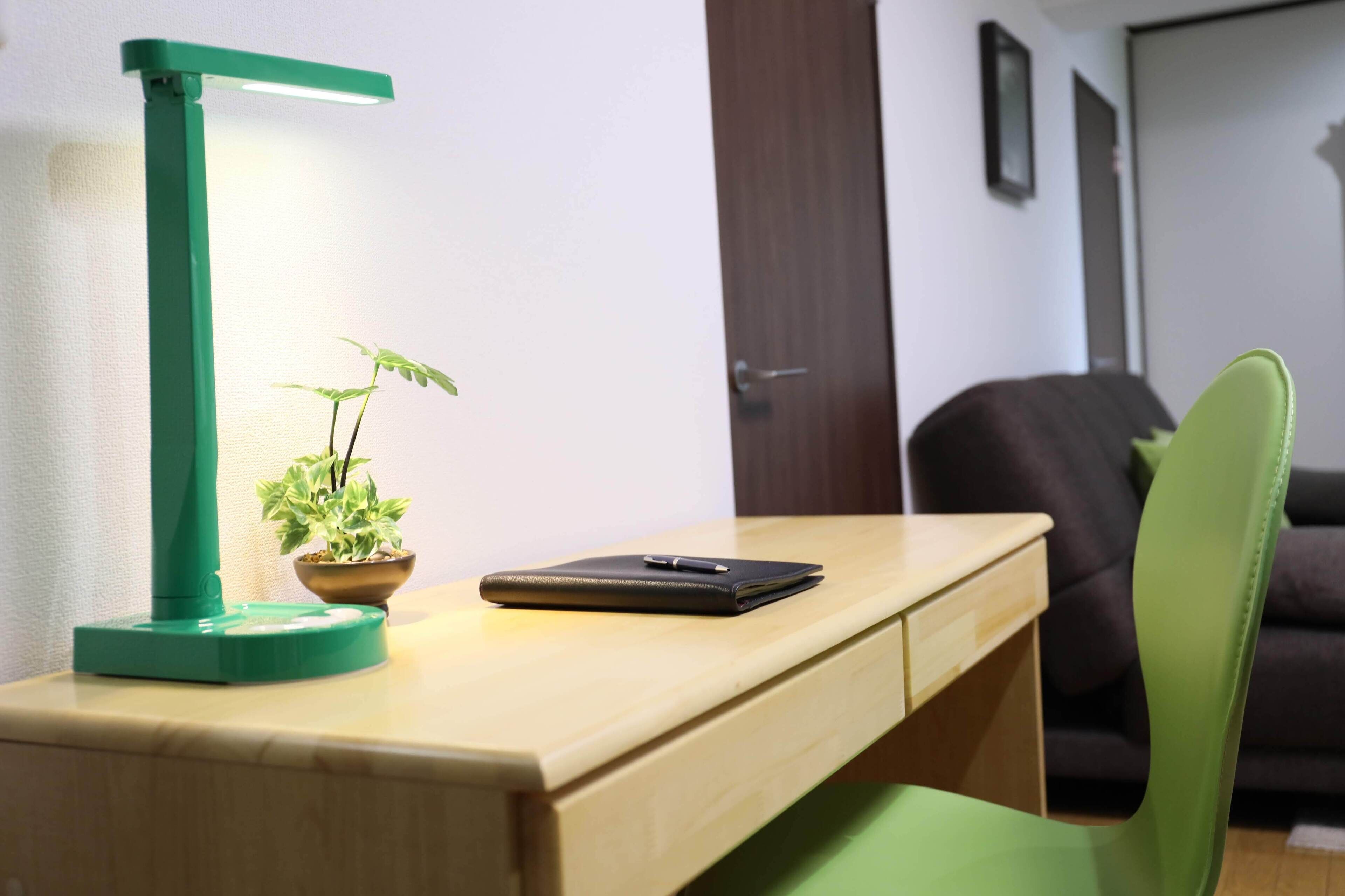 A desk with a green desk lamp, a potted plant, and a notebook.