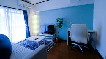 Une chambre d’hôtel moderne avec un canapé, une petite table, un téléviseur posé sur un meuble, un bureau avec une chaise et une plante en pot.