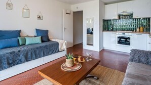 A modern living room with a sofa, a wooden coffee table, and a kitchen area with white cabinets and a green backsplash. - Village de Légenèse by Interhome (Carnac)