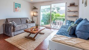 A living room with a grey sofa, a blue sofa, a wooden coffee table, and a large window with a view of greenery. - Village de Légenèse by Interhome (Carnac)