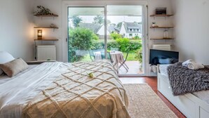 A bedroom with a bed, a TV, and a balcony with a view of houses and greenery. - Village de Légenèse by Interhome (Carnac)
