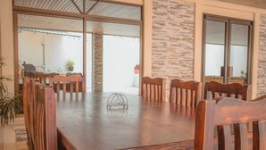 A spacious dining area with a large wooden table and chairs, a stone wall, and large windows. - The Amazing Home in a Small Town (Provincia de Alajuela)