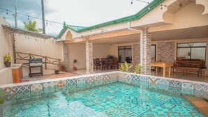 A swimming pool with patterned tiles, a covered patio area with seating, and a stone wall. - The Amazing Home in a Small Town (Provincia de Alajuela)