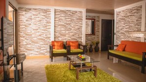 A living room with a brick-patterned wall, two sofas with orange cushions, a glass coffee table, and a green rug. - The Amazing Home in a Small Town (Provincia de Alajuela)