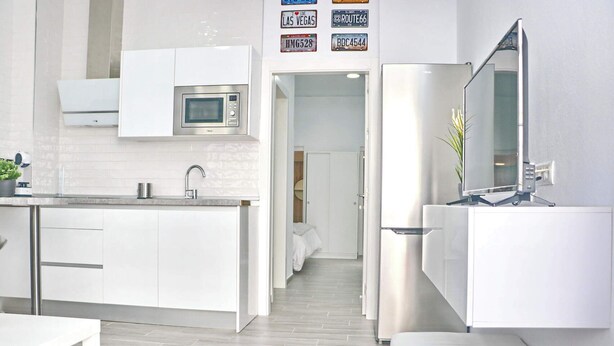 A modern kitchen with white cabinetry, a built-in microwave, and a stainless steel refrigerator. There is a small sink with a mirror above it, and a potted plant on the counter. - Apartment Isabella Vejer (Vejer de la Frontera)