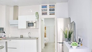 A modern kitchen with white cabinetry, a microwave, a sink, and a refrigerator. There are decorative license plates on the wall and a plant on the counter. - Apartment Isabella Vejer (Vejer de la Frontera)