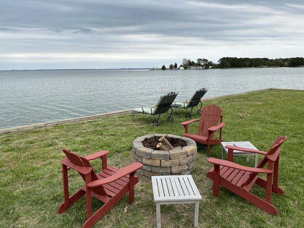 A lakeside seating area with Adirondack chairs and a fire pit.
