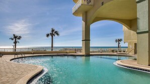 Une piscine avec vue sur l’océan, des palmiers et un bâtiment doté d’un balcon.