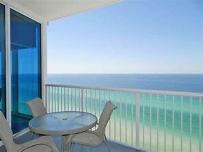 Un balcon doté d’une porte vitrée, d’une table ronde et de deux chaises, offrant une vue dégagée sur l’océan.