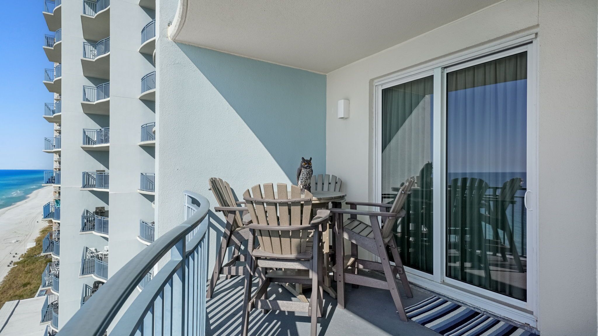 A balcony with a table and chairs, overlooking a beach and a high-rise building.