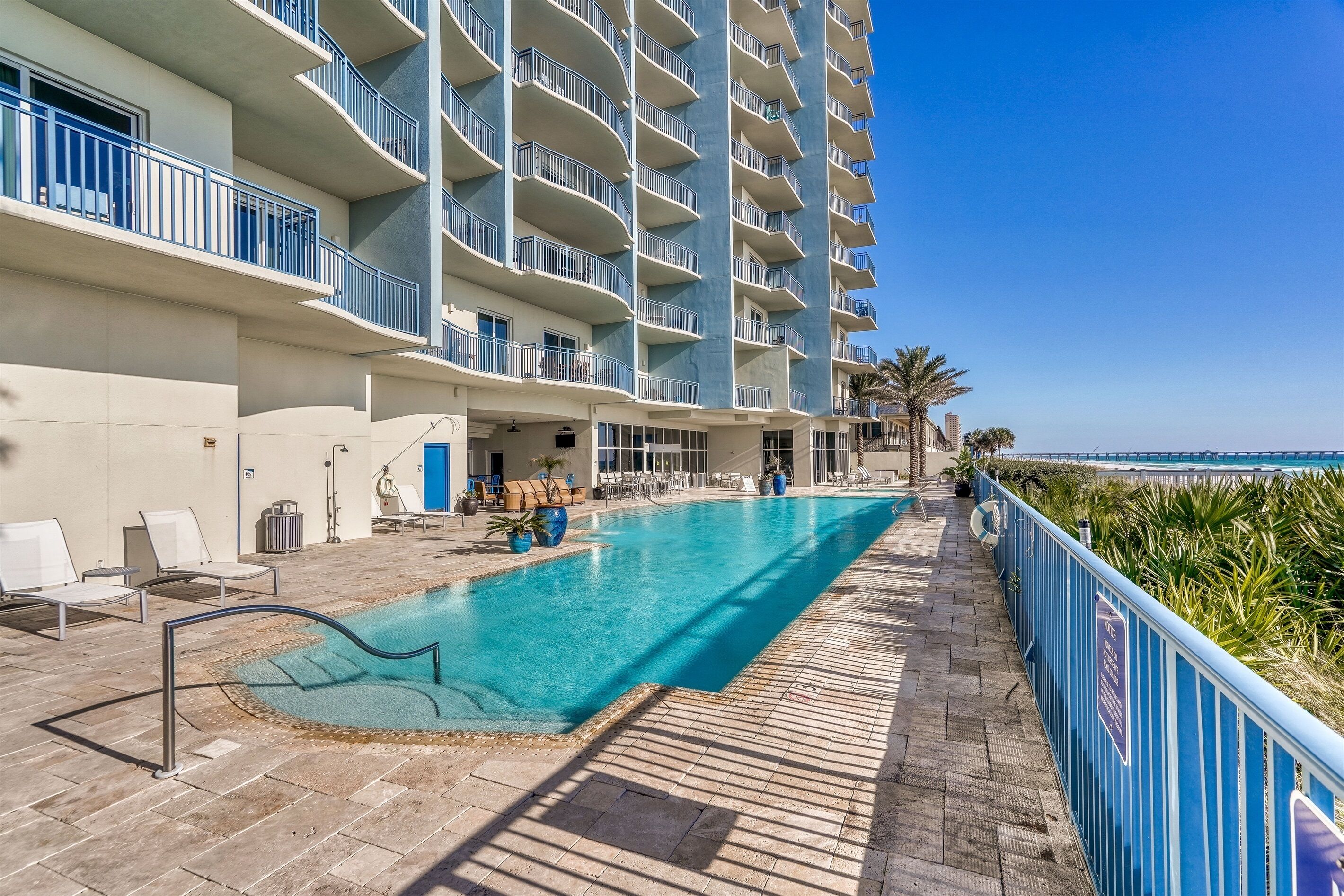 Un espace piscine d’hôtel offrant une vue dégagée sur l’océan, une piscine avec un plongeoir et un balcon doté d’une balustrade.