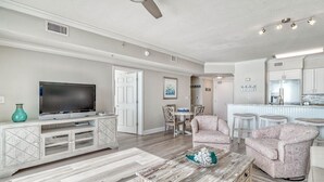 A modern living room with a flat-screen TV, a coffee table, patterned chairs, a dining area, and a kitchen with white cabinets and a bar. - *Sept 6- 8th/Labor Day Open!* Beach chairs included! (Panama City Beach)