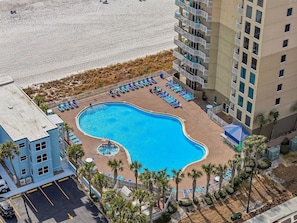 A swimming pool surrounded by lounge chairs, a building with balconies, and a parking area. - *July 12 - 15th available!* Beach chairs included! (Panama City Beach)