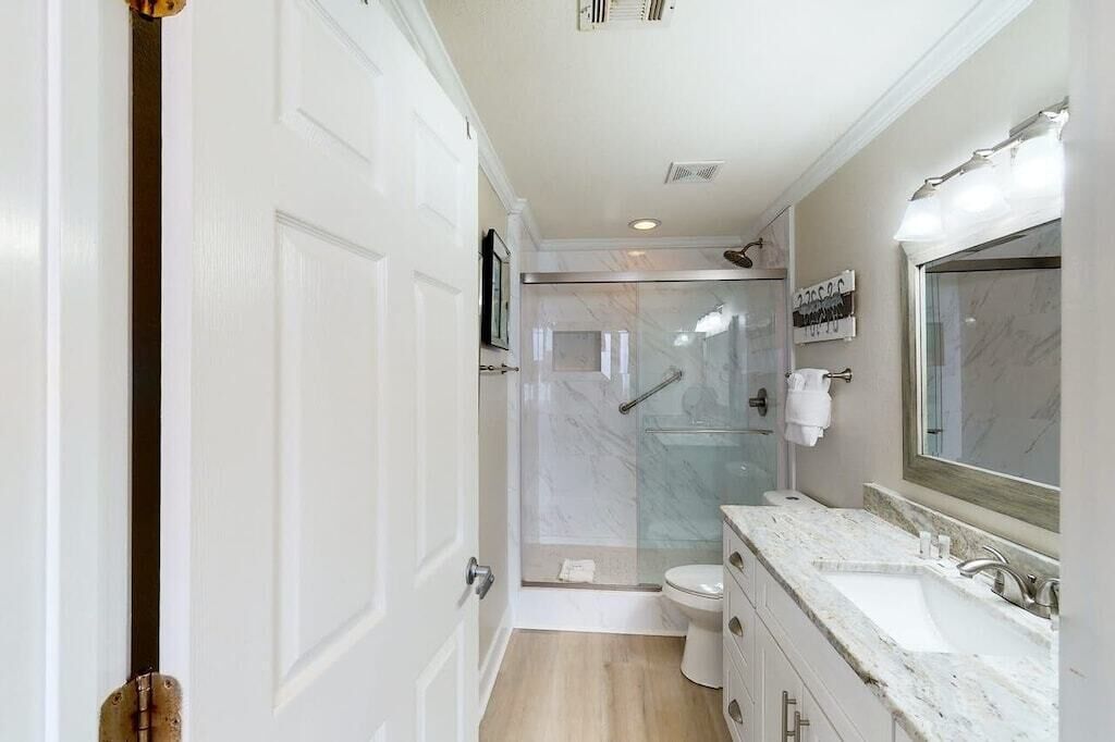 A modern bathroom with a glass-enclosed shower, a large mirror, and a marble countertop.