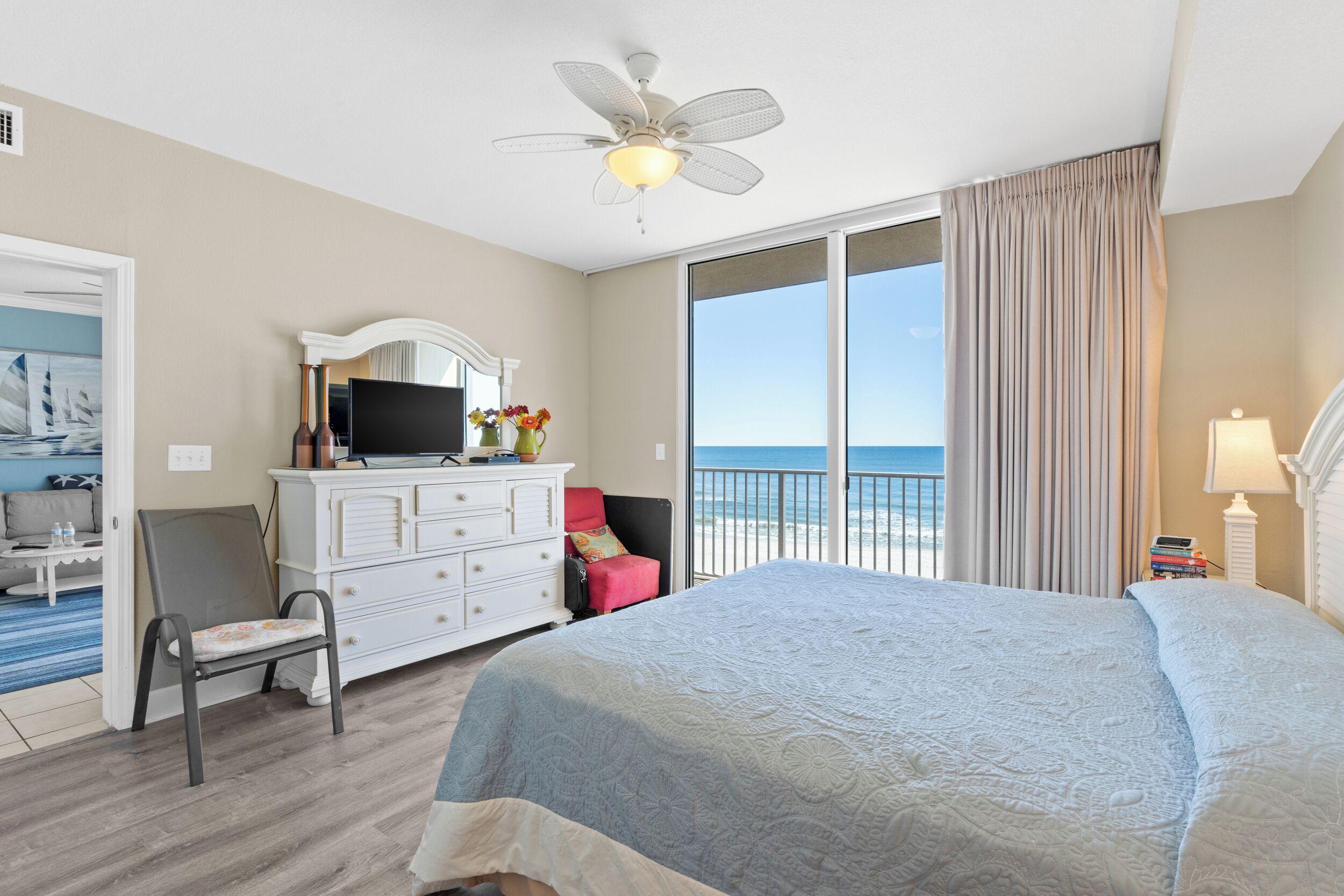 A hotel room with a bed, a television on a dresser, a chair, a desk, and a view of the ocean.