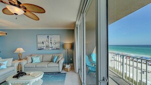 Un balcon avec vue sur la plage, un canapé, une table basse et un ventilateur de plafond.