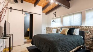 A bedroom with a large bed, a wooden ceiling, a brick wall, and a window with blinds. - Buckhead Battle House - an MCM architectural masterpiece (Atlanta)