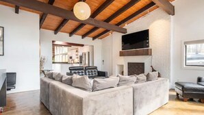 A spacious living area with a large sectional sofa, a fireplace, and a television mounted on the wall. - Buckhead Battle House - an MCM architectural masterpiece (Atlanta)