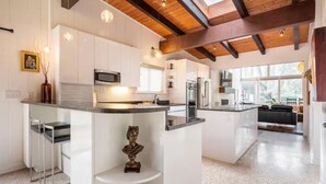 A modern kitchen with white cabinetry, a central island, and a wooden ceiling. - Buckhead Battle House - an MCM architectural masterpiece (Atlanta)