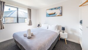 A hotel room with a large bed, a bedside table with a lamp, a painting on the wall, and a window with curtains.