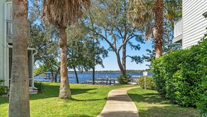 A pathway leading to a dock by a lake, surrounded by trees and a building. - Sleeps 6- 2 bedrooms with private baths, crib, bay access, pool, mins to Beach! (Navarre)