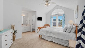 A bedroom with a bed, a ceiling fan, a window with curtains, a TV on the wall, and a bathroom visible in the background. - Sleeps 6- 2 bedrooms with private baths, crib, bay access, pool, mins to Beach! (Navarre)