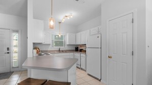A modern kitchen with white cabinets, a central island, and pendant lighting. - Sleeps 6- 2 bedrooms with private baths, crib, bay access, pool, mins to Beach! (Navarre)
