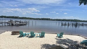A sandy beach with turquoise Adirondack chairs and a wooden deck. - Sleeps 6- 2 bedrooms with private baths, crib, bay access, pool, mins to Beach! (Navarre)