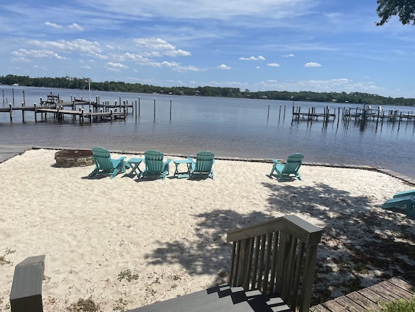 A sandy beach with turquoise Adirondack chairs and a wooden deck.