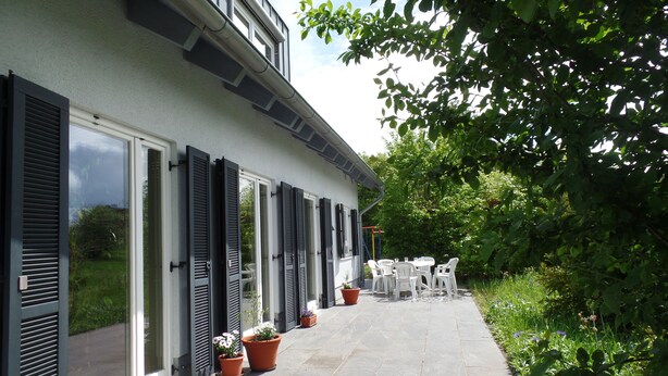 Ein Haus mit überdachter Terrasse, Blumentöpfen und Gartenmöbeln.