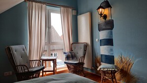 Ein Zimmer mit einem Bett, zwei gestreifte Stühle, einem kleinen Tisch, einem Fenster mit Vorhängen, einer Wandlampe und einer Heizung.
