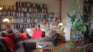 Ein gemütliches Wohnzimmer mit einem Ecksofa, einem kleinen Couchtisch mit Büchern und einer Bücherwand voller Bücher.