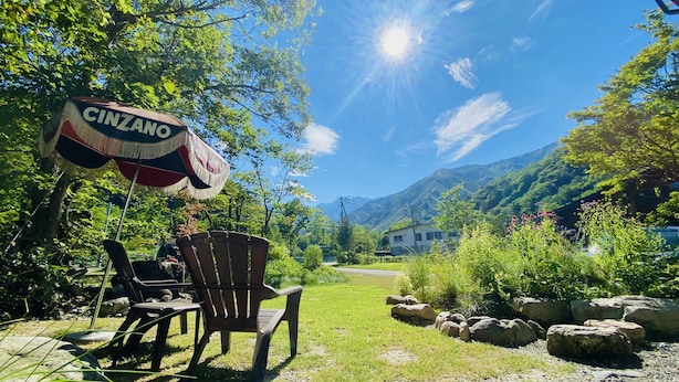 An outdoor seating area with a 'CINZANO' sign, wooden chairs, and a mountain backdrop. - AGS Trailer House - Campground (Hakuba)