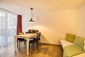 Une pièce comprenant une table à manger, des chaises, un four à micro-ondes, un canapé avec un coussin vert et une fenêtre avec des rideaux.