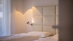 Una cama bien hecha con cabecera, lámpara de noche y ventana con cortinas traslúcidas.