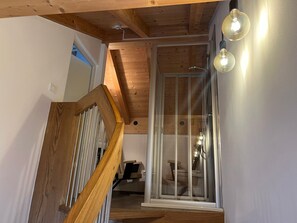 Una escalera de madera que conduce a una puerta de cristal, una cámara de seguridad instalada en el techo y un aplique fijado a la pared.