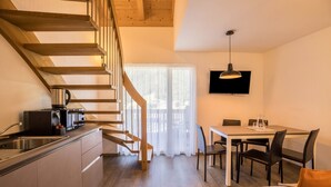 Una cocina moderna con una escalera de madera, una zona de comedor con mesa y sillas, y un televisor montado en la pared.