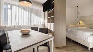 A modern room with a dining table, chairs, a bed, and a TV. - Holiday Apartment "Dui Residenz Bun Sté" with Mountain View & Garden (San Vigilio di Marebbe)