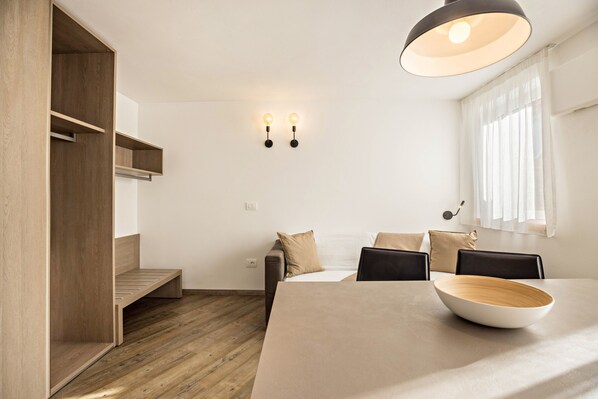 A modern room with a wooden floor, a bed with a headboard, a dining table with a bowl, and two wall-mounted lights.