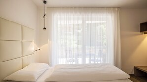 A modern bedroom with a large bed, a headboard with integrated lighting, a window with sheer curtains, and a small bedside table. - Apartment Treï Residence Bun Sté with Mountain View, Sauna, Wi-Fi, Terrace & Balcony (San Vigilio di Marebbe)