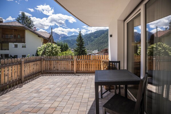 A balcony with a table and chairs, a wooden fence, and a mountain view.