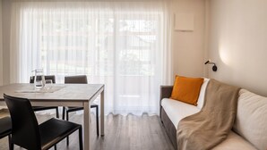 A room with a dining table, chairs, a sofa, a throw blanket, and a window with sheer curtains. - Apartment Treï Residence Bun Sté with Mountain View, Sauna, Wi-Fi, Terrace & Balcony (San Vigilio di Marebbe)