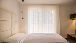 Ein Schlafzimmer mit einem Bett, einem Kopfteil, einem Nachttisch und einem Fenster mit durchsichtigen Vorhängen.