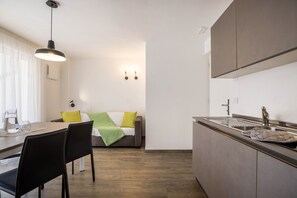 A modern kitchen with a built-in sink, a dining area with a table and chairs, and a sofa with cushions.