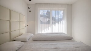 A modern bedroom with a large bed, a headboard, and a window with sheer curtains. - Apartment "Set Residenz Bun Sté" with Mountain View, Sauna & Balcony (San Vigilio di Marebbe)