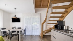 A modern kitchen with a wooden staircase, a dining area with a table and chairs, and a flat-screen TV mounted on the wall. - Apartment "Set Residenz Bun Sté" with Mountain View, Sauna & Balcony (San Vigilio di Marebbe)