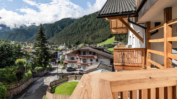 A residential area with a wooden balcony, a stone wall, and a view of a mountain. - Apartment "Set Residenz Bun Sté" with Mountain View, Sauna & Balcony (San Vigilio di Marebbe)