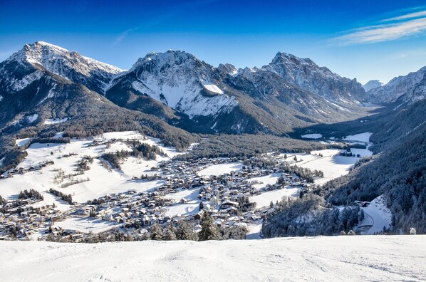 Un pueblo cubierto de nieve en las montañas, con edificios, una pista de esquí y un valle.